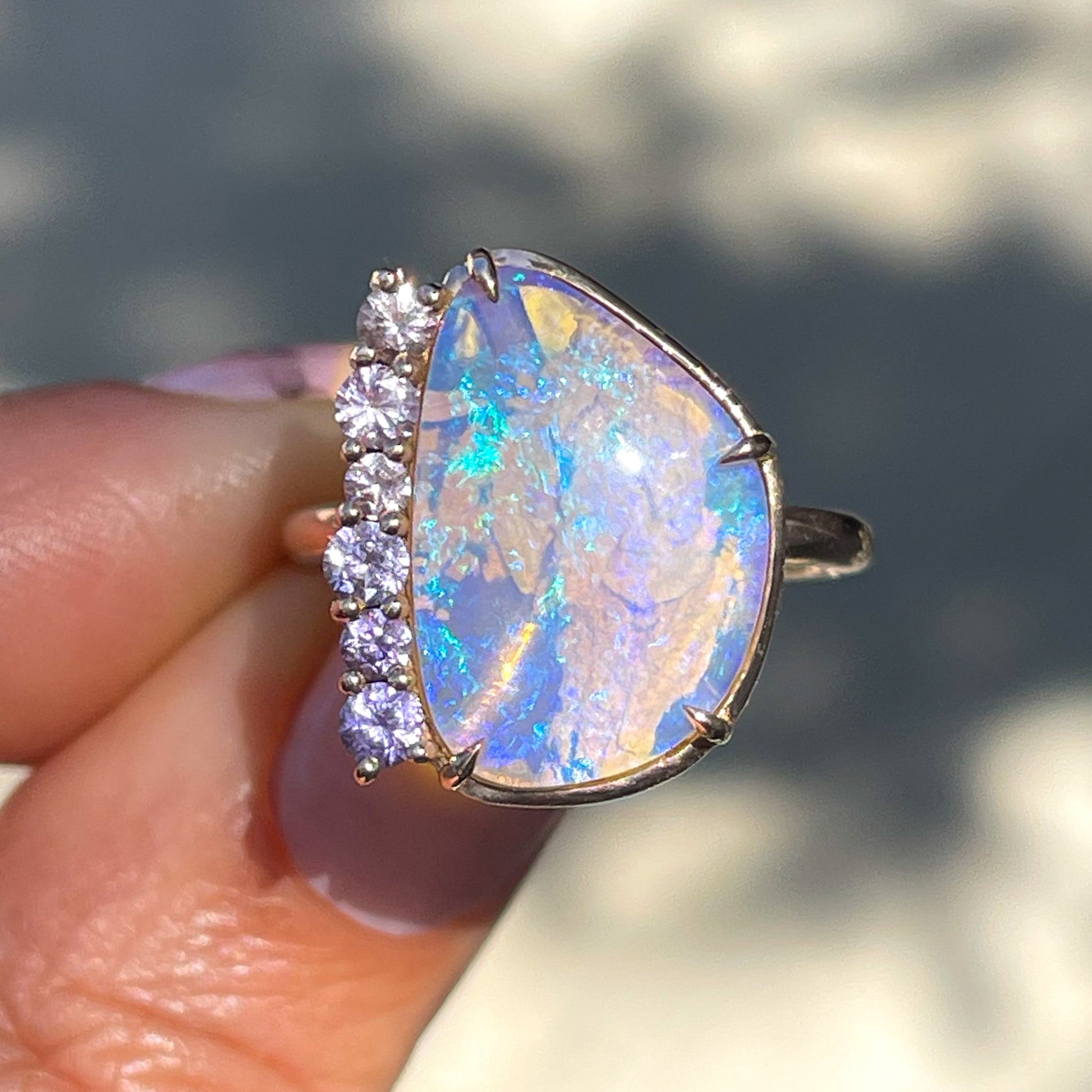 An Australian Opal Ring by NIXIN Jewelry held in sunlight. One of the best opal rings with a Crystal Opal and assorted sized sapphires.