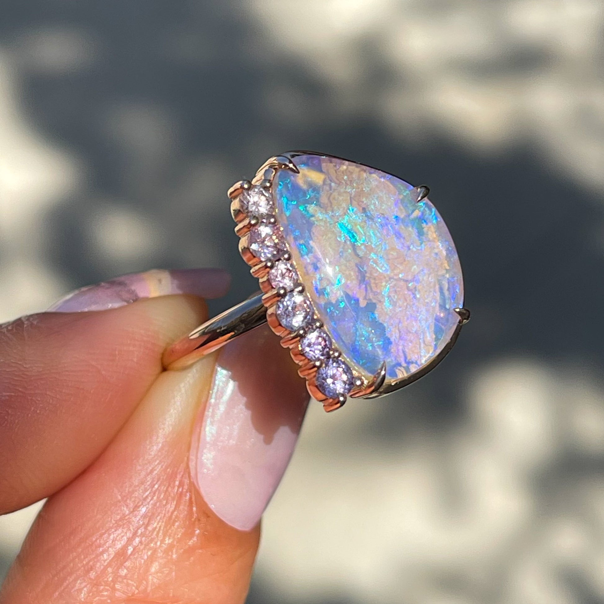 An Australian Opal Ring by NIXIN Jewelry held at an angle to show the prong setting of the sapphire frame. The purple opal flashes electric blue sparks across its facade.