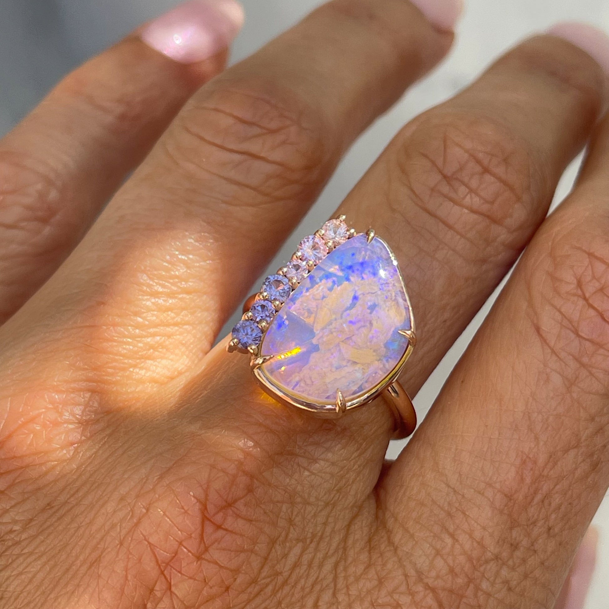 An Australian Opal Ring by NIXIN Jewelry modeled on a hand. The lavender opal ring is decorated with beautiful pink and purple sapphires.