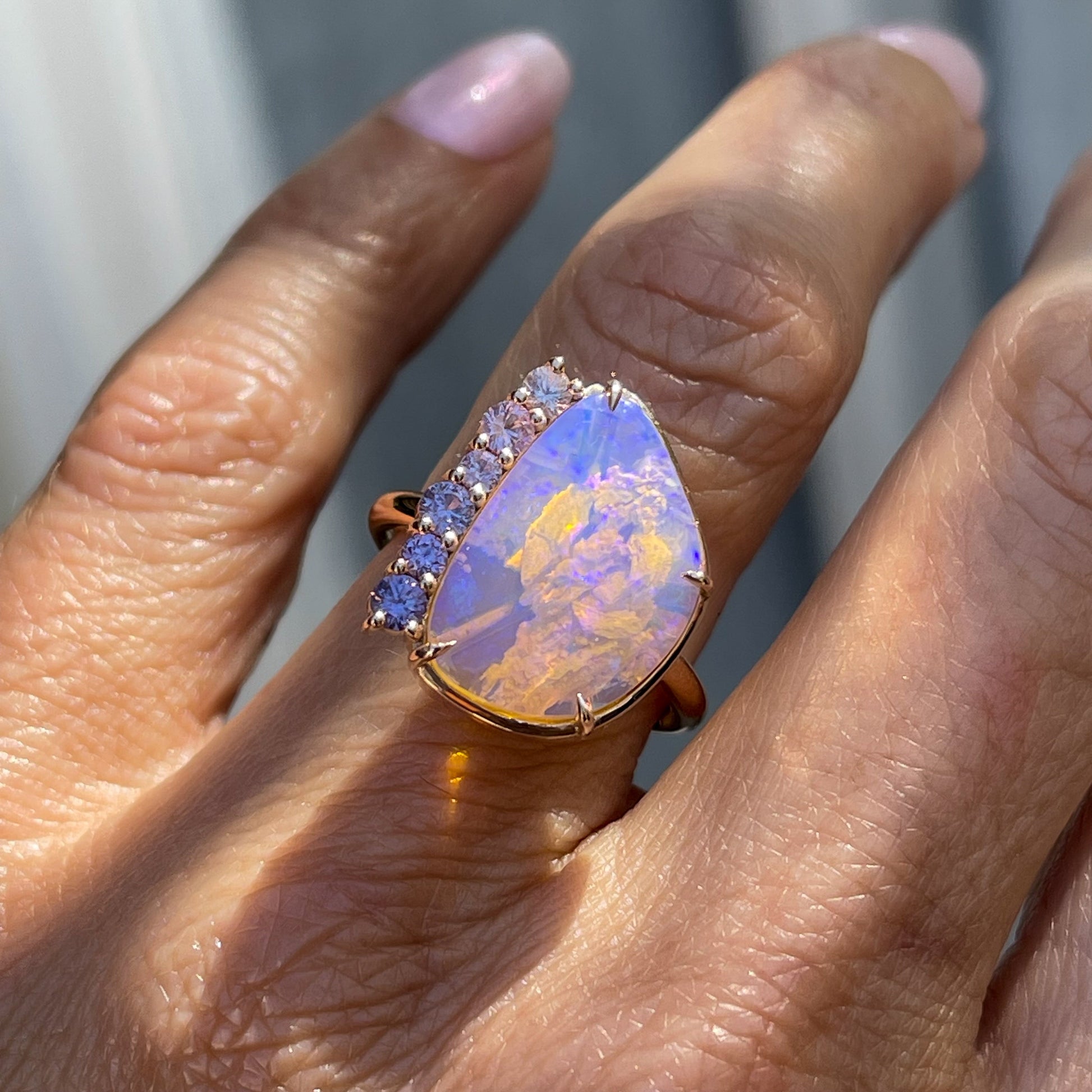 An Australian Opal Ring by NIXIN Jewelry modeled on a hand. One of the opal rings for sale on NIXINJewelry.com, this ring has an opal stone bordered by pink and purple sapphires.