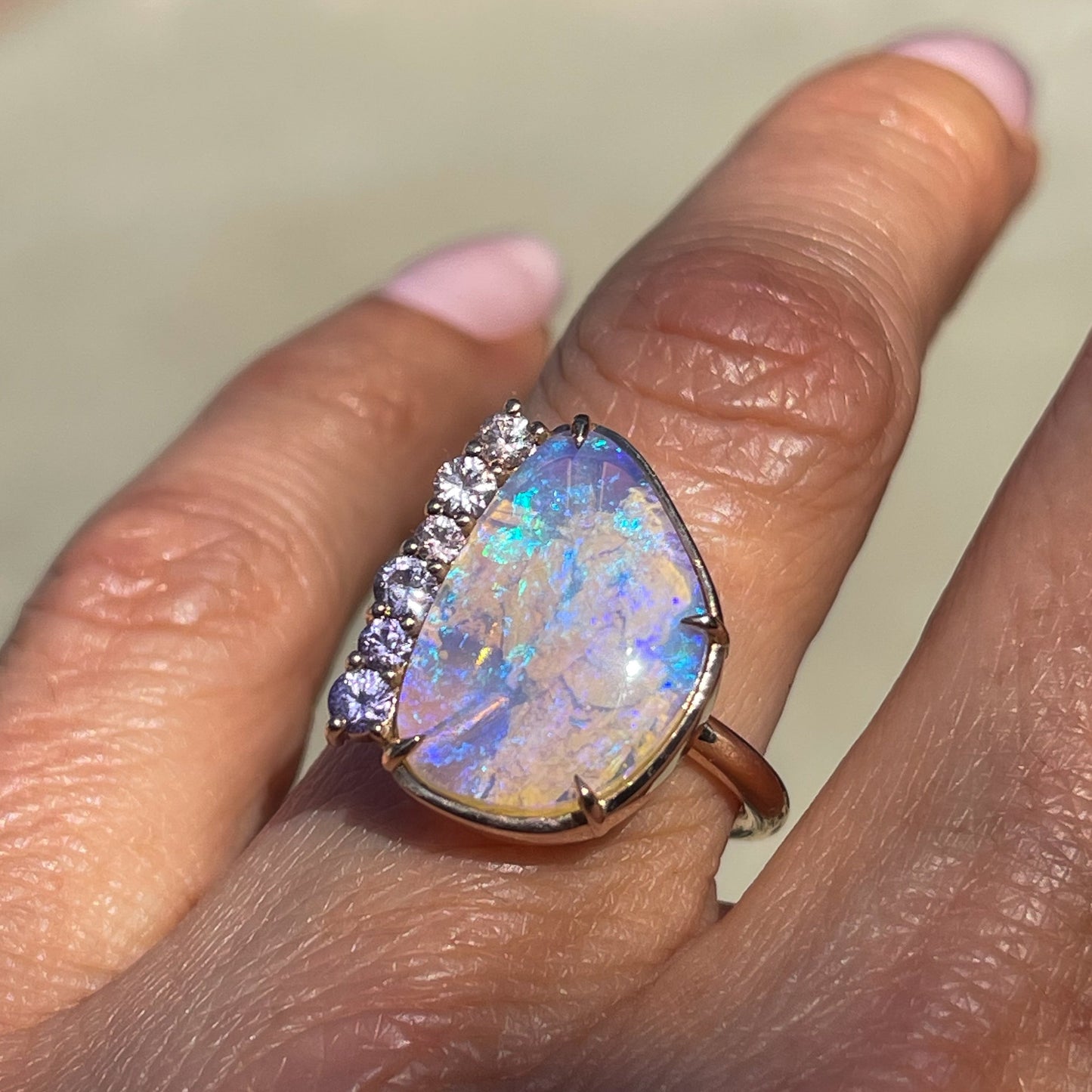 An Australian Opal Ring by NIXIN Jewelry modeled on a hand. The rose gold opal ring is a beautiful example of unique opal jewelry.
