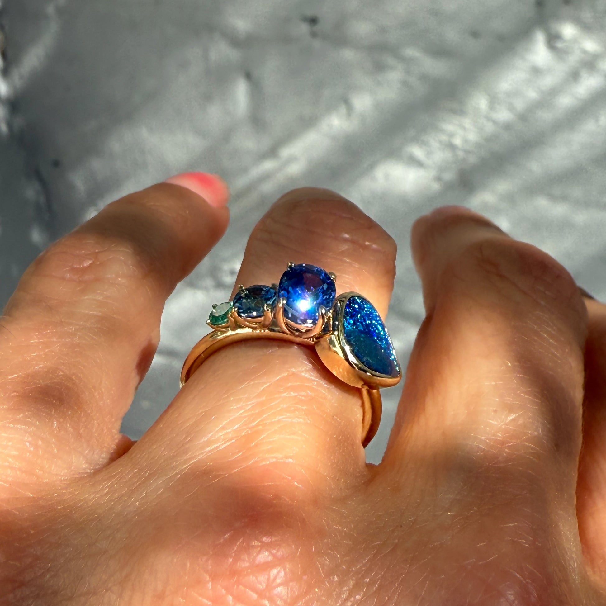 Angled view of an Australian Opal Ring by NIXIN Jewelry. This black opal ring is a true jewelry art piece, worn on a hand, highlighting the captivating play-of-color in the opal and sapphire side stones.