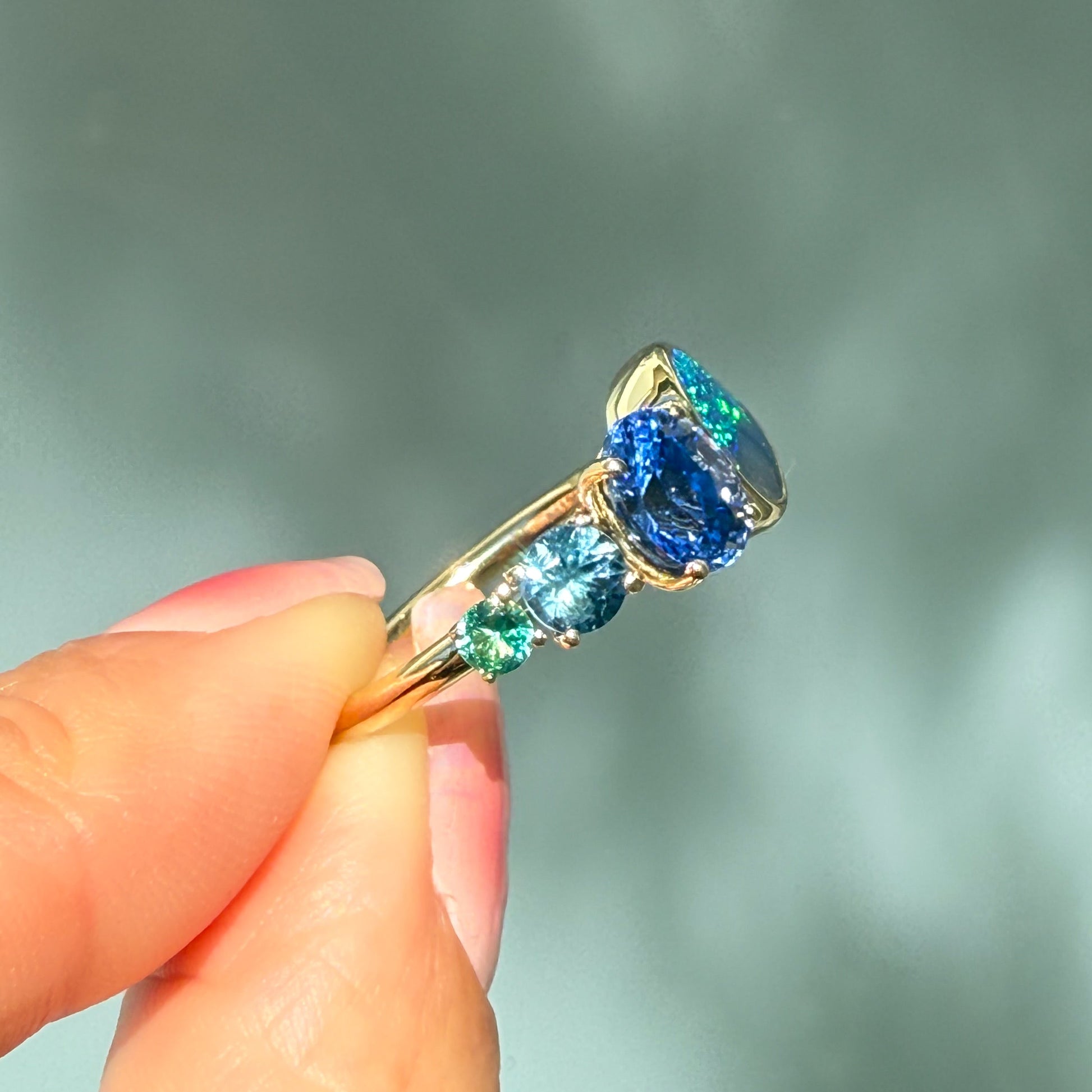 An Australian Opal Ring by NIXIN Jewelry. The rare opal jewelry piece is held from the side, showcasing the clean lines of the setting and the meticulous detail of the prong setting and bezel settings for each opal stone.