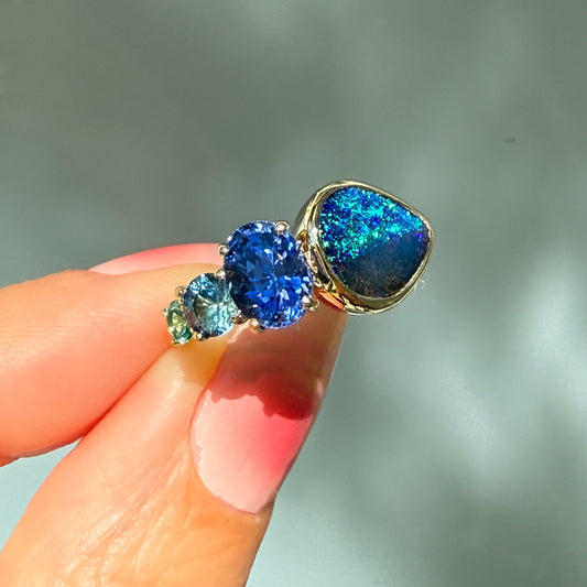 An Australian Opal Ring by NIXIN Jewelry. The luxury ring is shown from a different angle, highlighting the contrast between the dual-patterned black opal and the stunning sapphire opal ring combination.