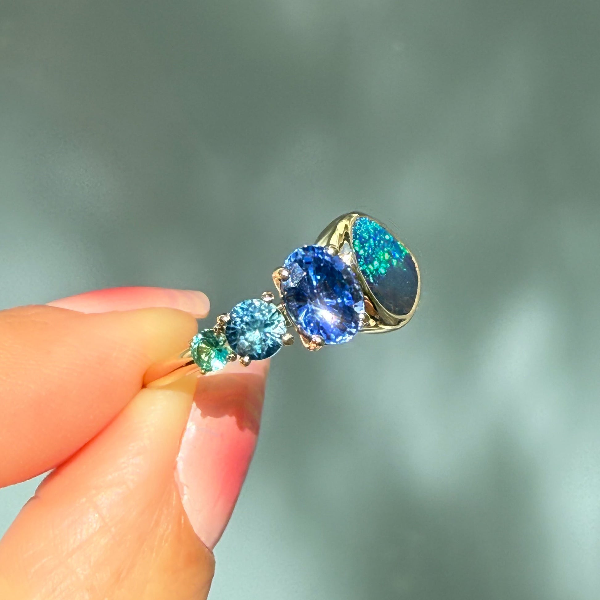 An Australian Opal Ring by NIXIN Jewelry. The ring is held at an angle that catches the light, showing the exceptional color and brilliance of the lightning ridge opal ring. This is a truly unique jewelry creation.