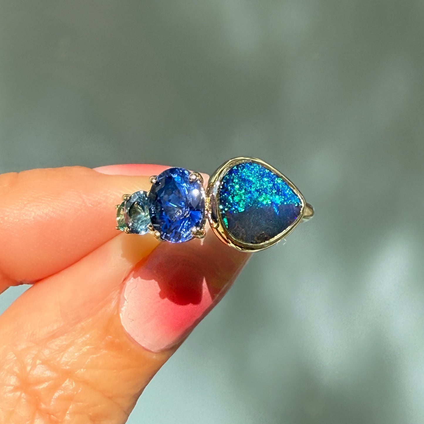 An Australian Opal Ring by NIXIN Jewelry. This rare opal ring features a vibrant blue black opal and an ombré sapphire trio, set in a unique fine jewelry design.