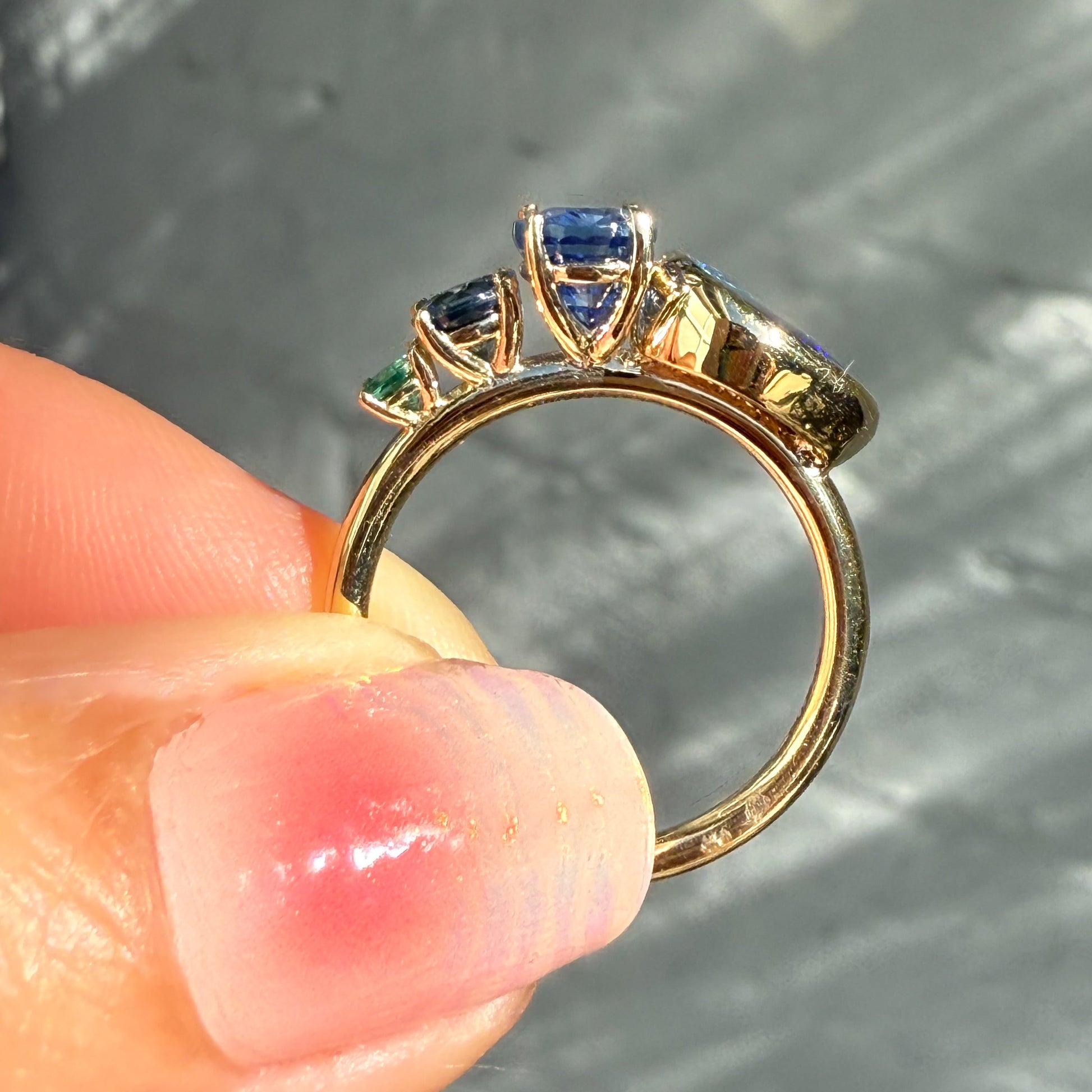 An Australian Opal Ring by NIXIN Jewelry. The rare opal jewelry piece is held from the side, showcasing the clean lines of the setting and the meticulous detail of the prong and bezel settings for each opal stone.