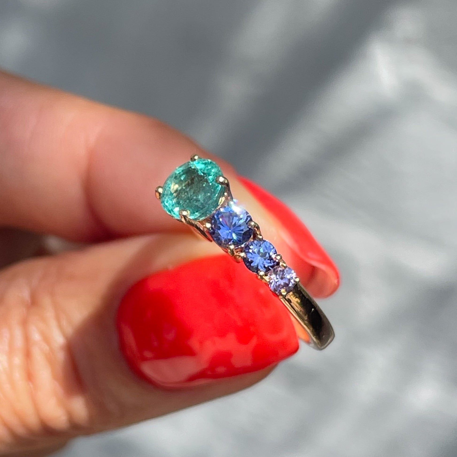 A Colombian Emerald Ring by NIXIN Jewelry held in sunlight showing its sapphire side. The opposite side of this emerald and purple sapphire ring has a row of pave diamonds.