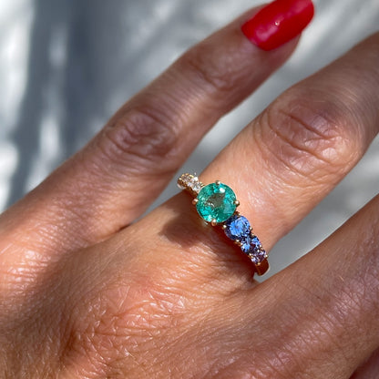 A Colombian Emerald Ring by NIXIN Jewelry is modeled on the hand. With purple sapphires and pave diamonds the emerald wedding ring is the perfect find for beautifully unique jewelry.