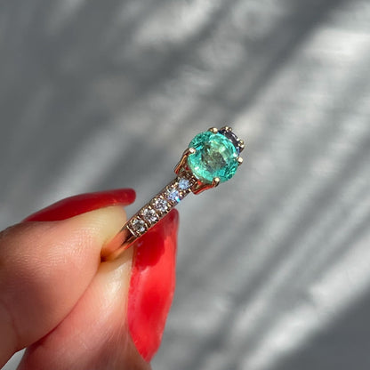 A Colombian Emerald Ring by NIXIN Jewelry held in sunlight to show one side of its asymmetrical design. The emerald diamond ring has ombré sapphires on the far side — a stunning piece of couture jewelry.
