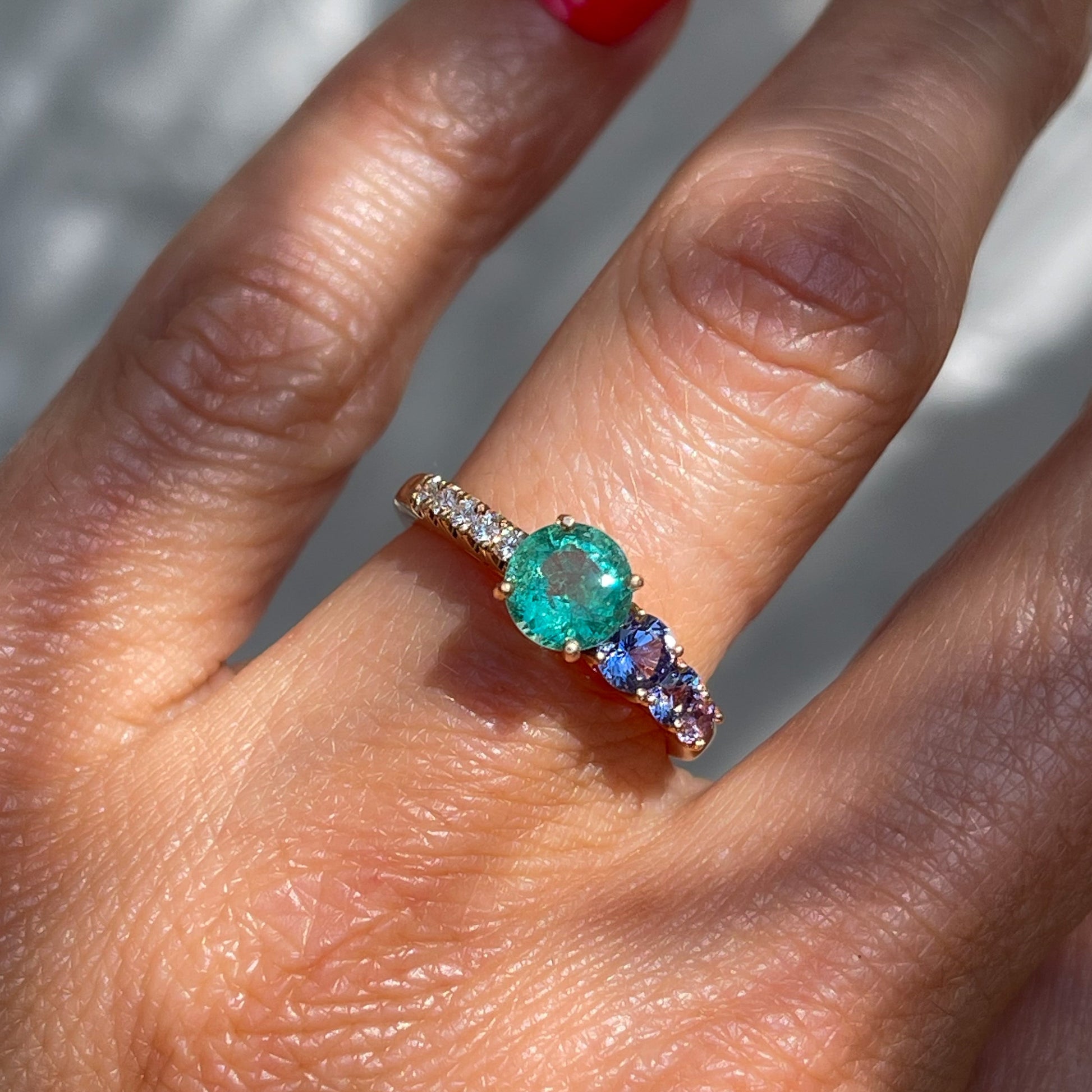 A Colombian Emerald Ring by NIXIN Jewelry modeled on a hand. Made in rose gold with purple sapphires and pave diamond. 