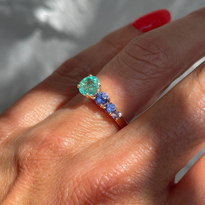 A Colombian Emerald Ring by NIXIN Jewelry worn on a hand. The unique emerald ring design includes purple and lavender sapphires set in rose gold.