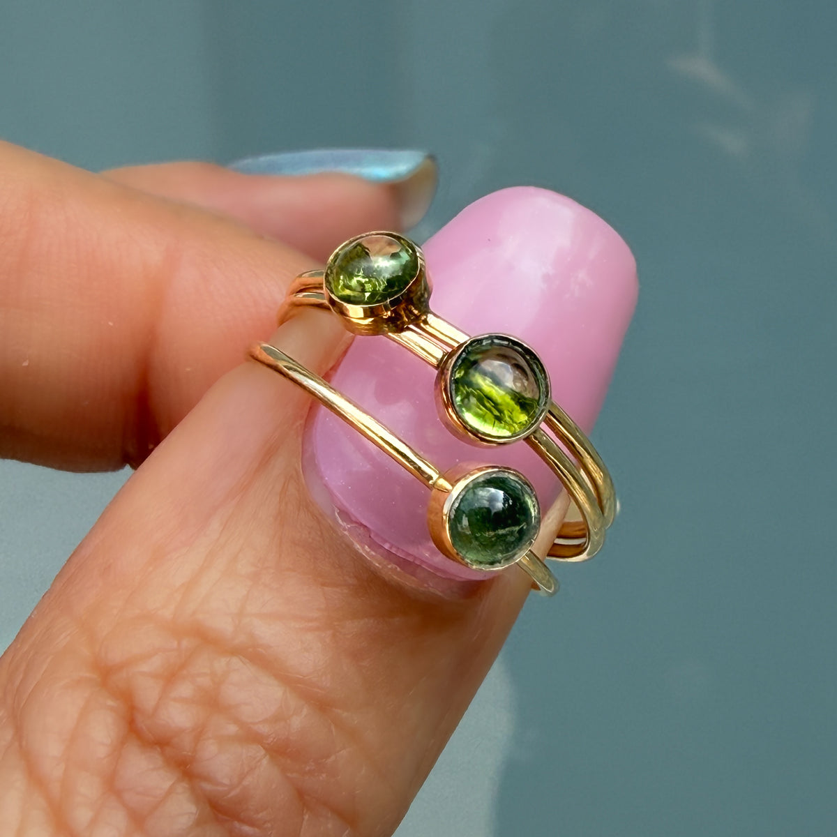 Lucky Green Tourmaline Rings held on a fingertip, three cabochon rings in 14k gold in olive, bright green and deep green.