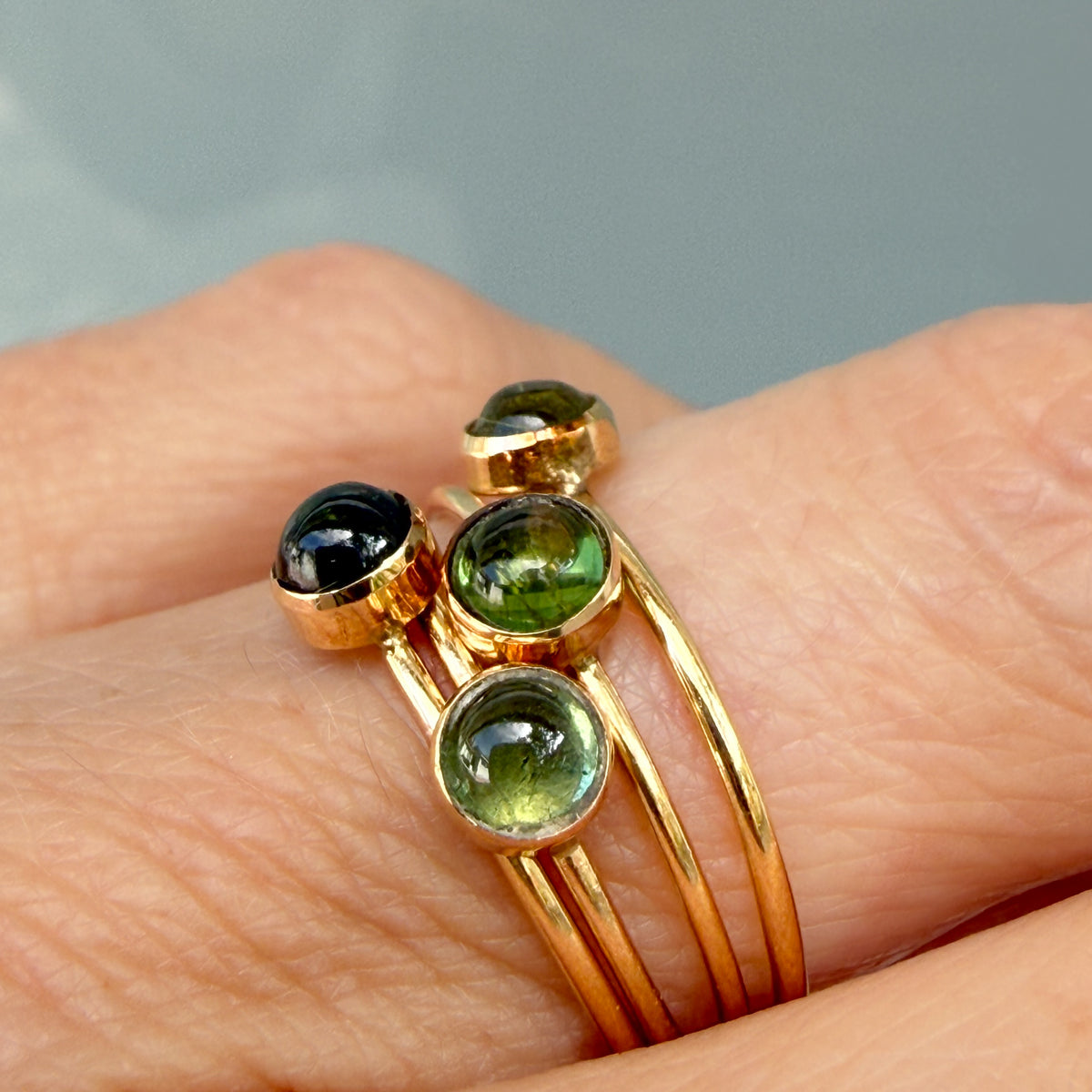 Lucky Green Tourmaline Rings in close-up, four tourmaline cabochons bezel set in 14k gold and stacked on one finger.