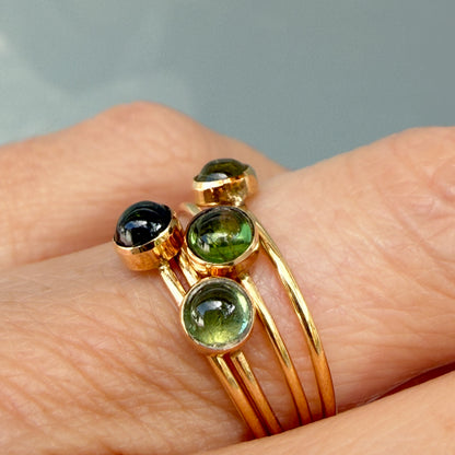 Lucky Green Tourmaline Rings in close-up, four tourmaline cabochons bezel set in 14k gold and stacked on one finger.