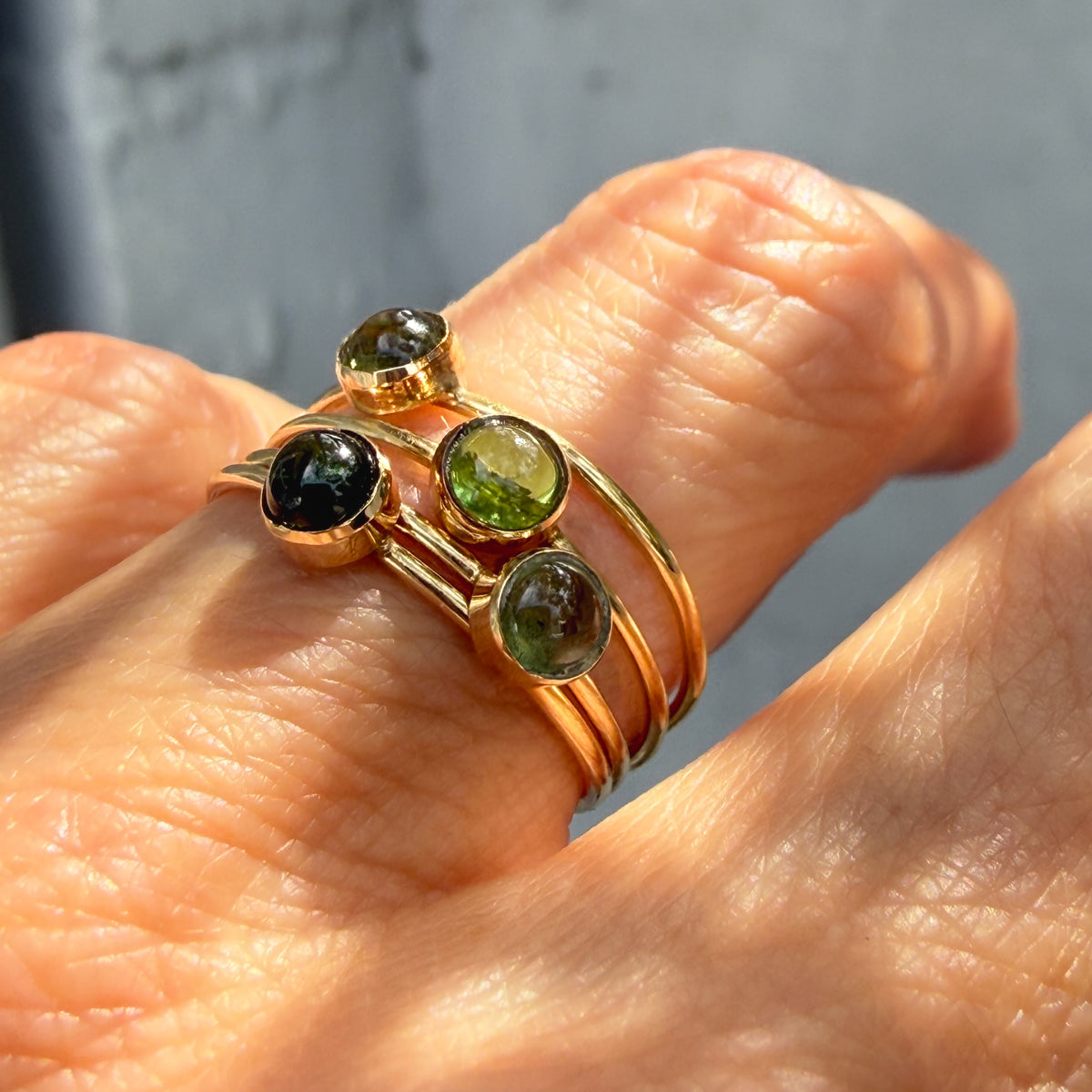Lucky Green Tourmaline Rings worn together in sunlight, handcrafted 14k gold stacking rings from pale chartreuse to deep green.