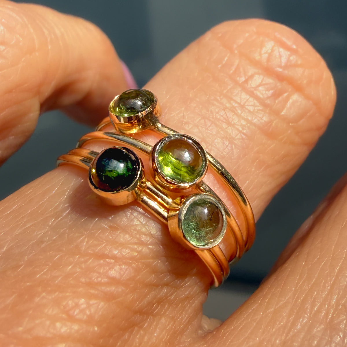 Lucky Green Tourmaline Rings stacked on one finger in warm light, four cabochons bezel set in 14k gold on slim bands.