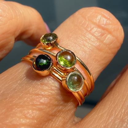 Lucky Green Tourmaline Rings stacked on one finger in warm light, four cabochons bezel set in 14k gold on slim bands.