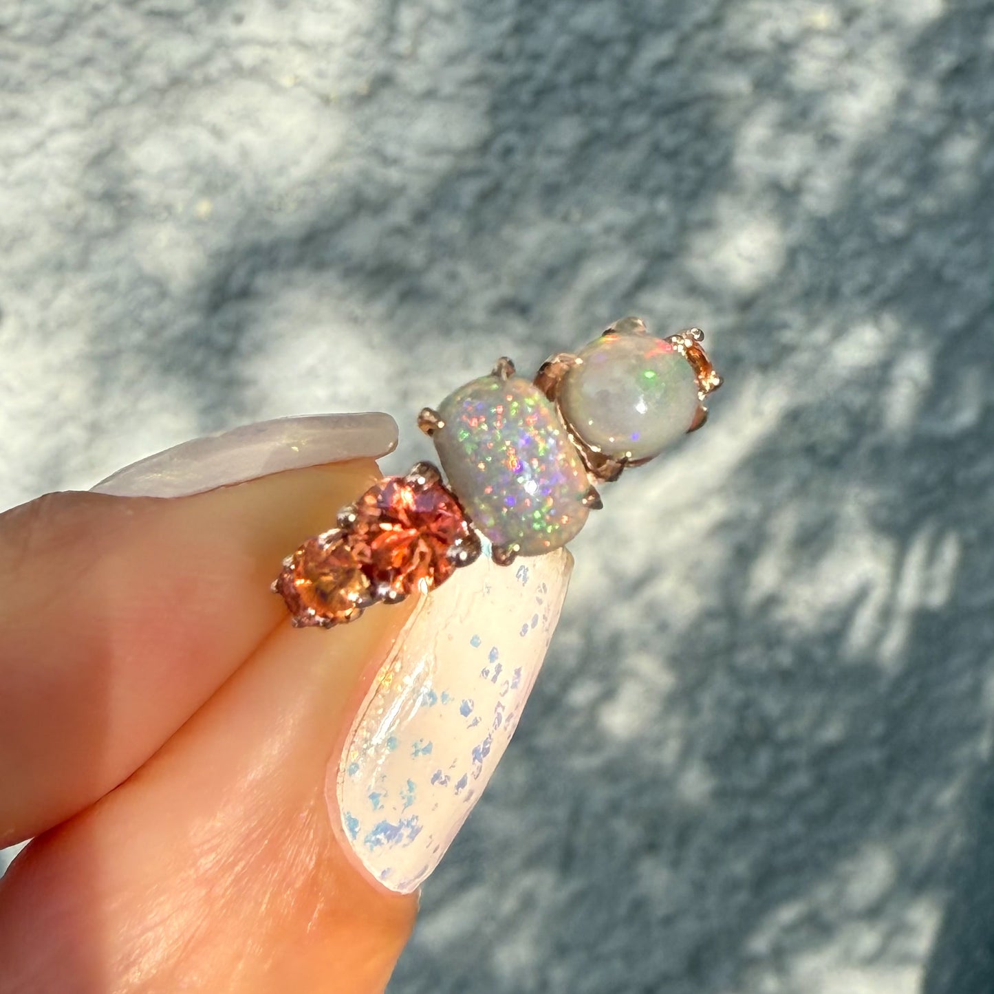 An Australian Opal Ring by NIXIN Jewelry showcasing the vivid peach ombre sapphires that flank the opals, creating a signature color story. The intense green and pink flash of the black opal jewelry defines its value as rare jewelry. This rose gold opal ring is a certified unique opal jewelry design.