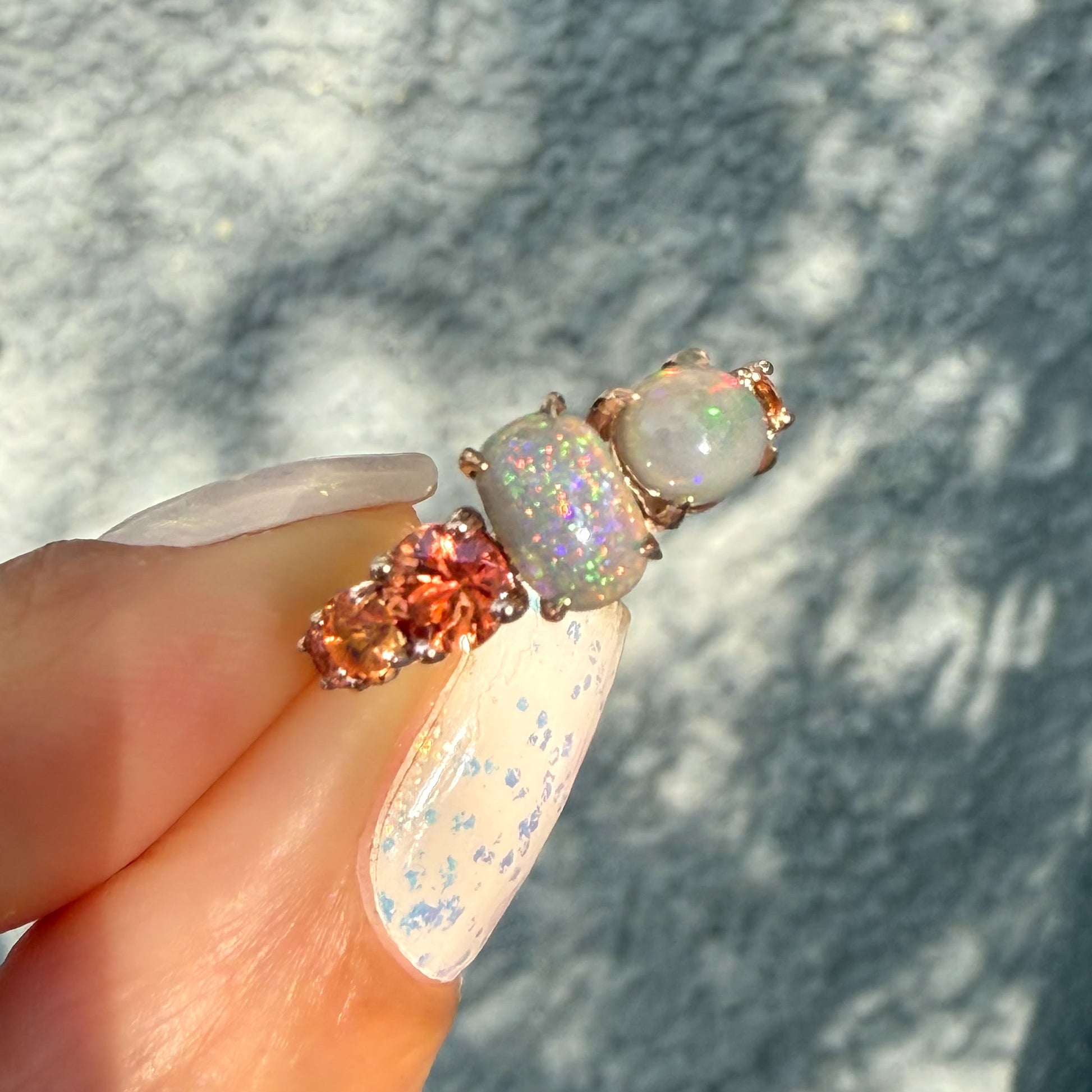 An Australian Opal Ring by NIXIN Jewelry showcasing the vivid peach ombre sapphires that flank the opals, creating a signature color story. The intense green and pink flash of the black opal jewelry defines its value as rare jewelry. This rose gold opal ring is a certified unique opal jewelry design.