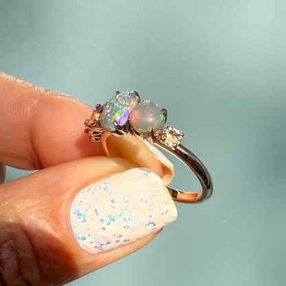 An Australian Opal Ring by NIXIN Jewelry held up to the light, showcasing the dual semi black opal cabochons. This rare opal jewelry features a beautiful contrast between pinfire and flash patterns, set in 14k rose gold. This unique fine jewelry is an exclusive luxury ring.