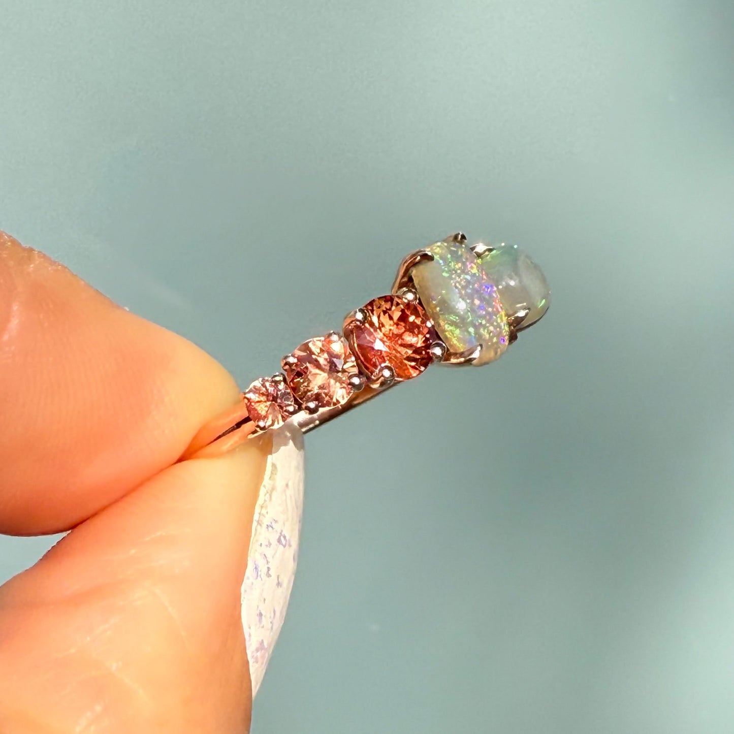 An Australian Opal Ring by NIXIN Jewelry viewed from the side, demonstrating the height and placement of the prong setting for maximum light exposure. The two lightning ridge opal gems are perfectly positioned with the contrasting sapphires. This women's luxury ring is guaranteed authentic australian opal.