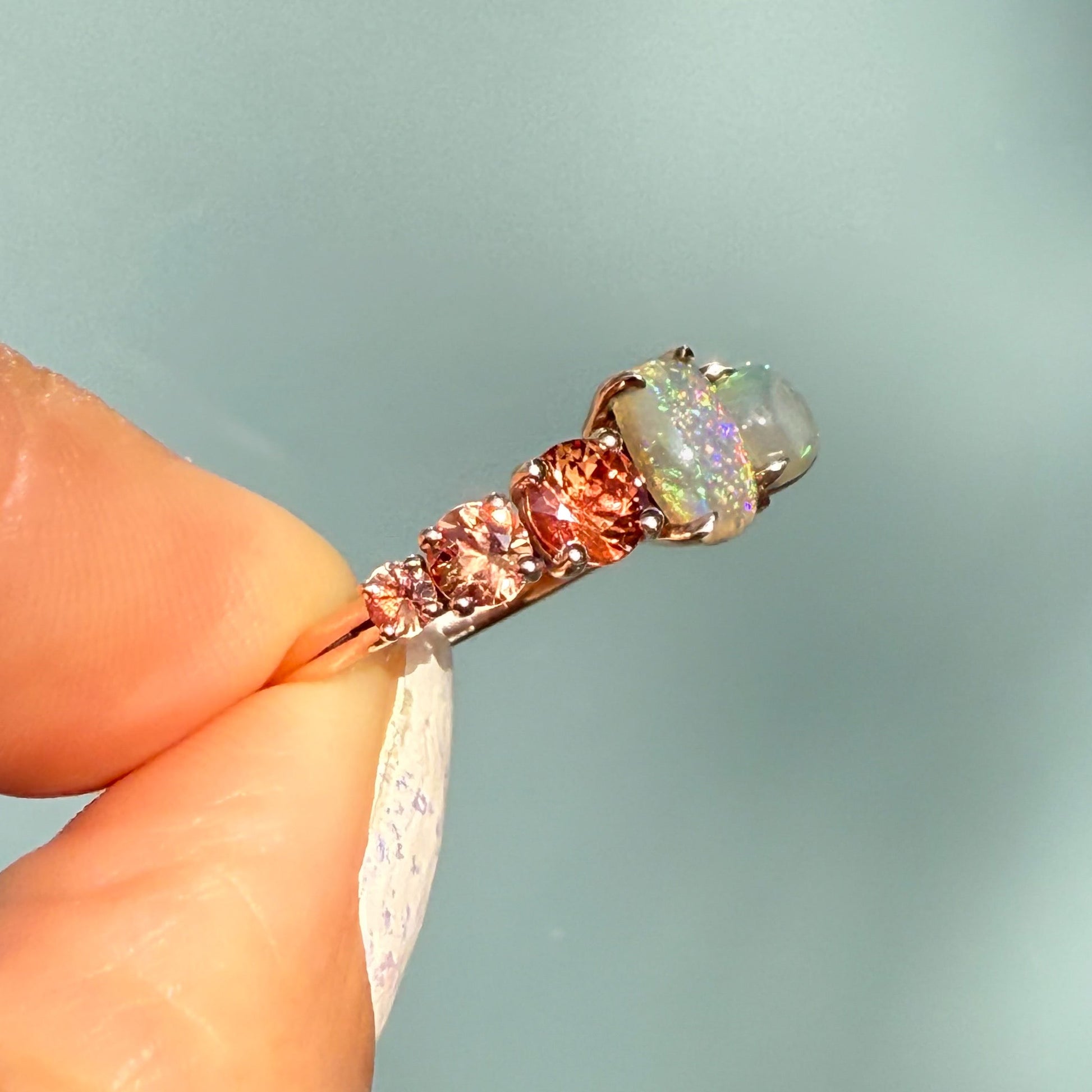 An Australian Opal Ring by NIXIN Jewelry viewed from the side, demonstrating the height and placement of the prong setting for maximum light exposure. The two lightning ridge opal gems are perfectly positioned with the contrasting sapphires. This women's luxury ring is guaranteed authentic australian opal.