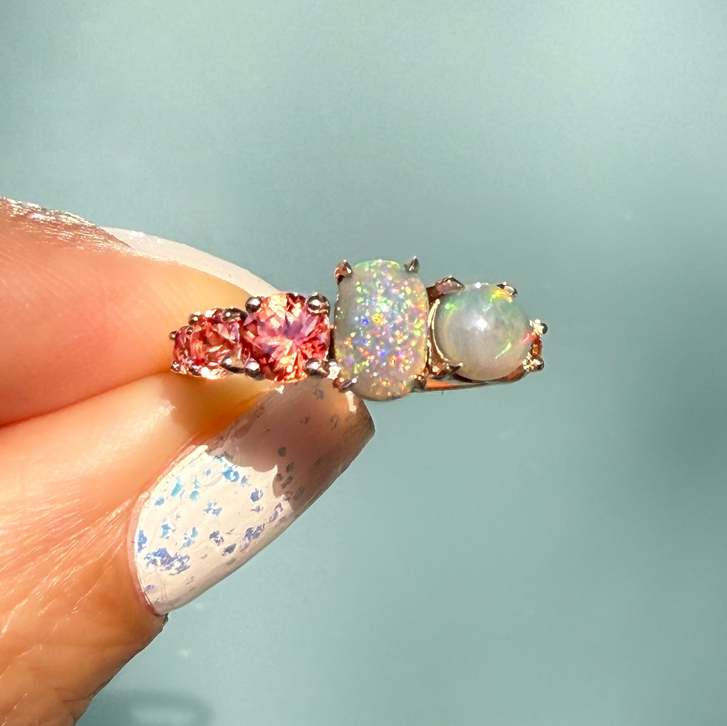 An Australian Opal Ring by NIXIN Jewelry showing an intense flash of pink and green across the natural opal black opal ring. The rare opal ring features flanking peach ombre sapphires in a clear size gradient. This close-up highlights the unique opal jewelry craftsmanship.