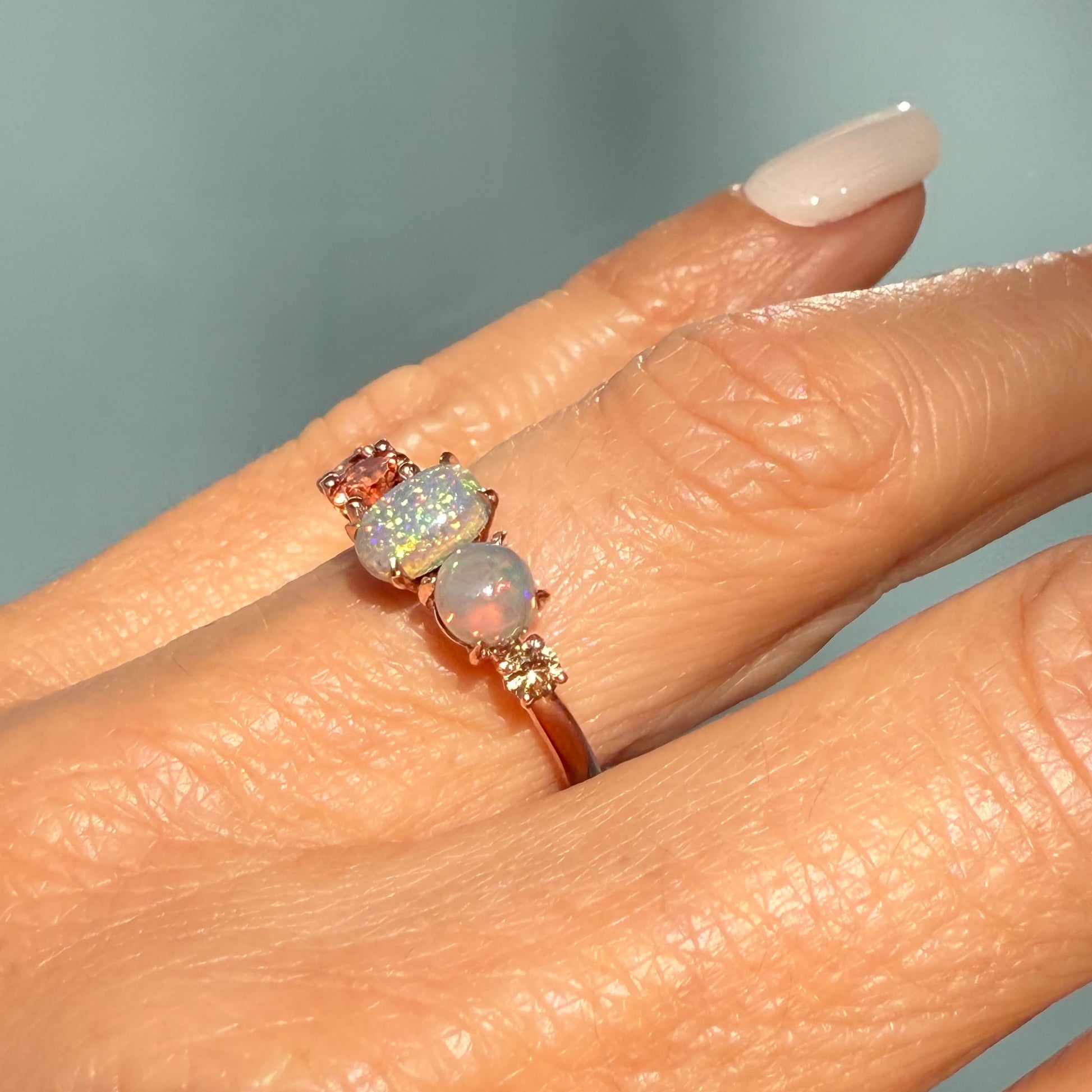 An Australian Opal Ring by NIXIN Jewelry highlighting the elegant curvature and warm hue of the 14k rose gold band. The rare jewelry features two distinct semi black opal patterns set among the ombre peach sapphires. This unique jewelry is a prime example of exceptional jewelry art.