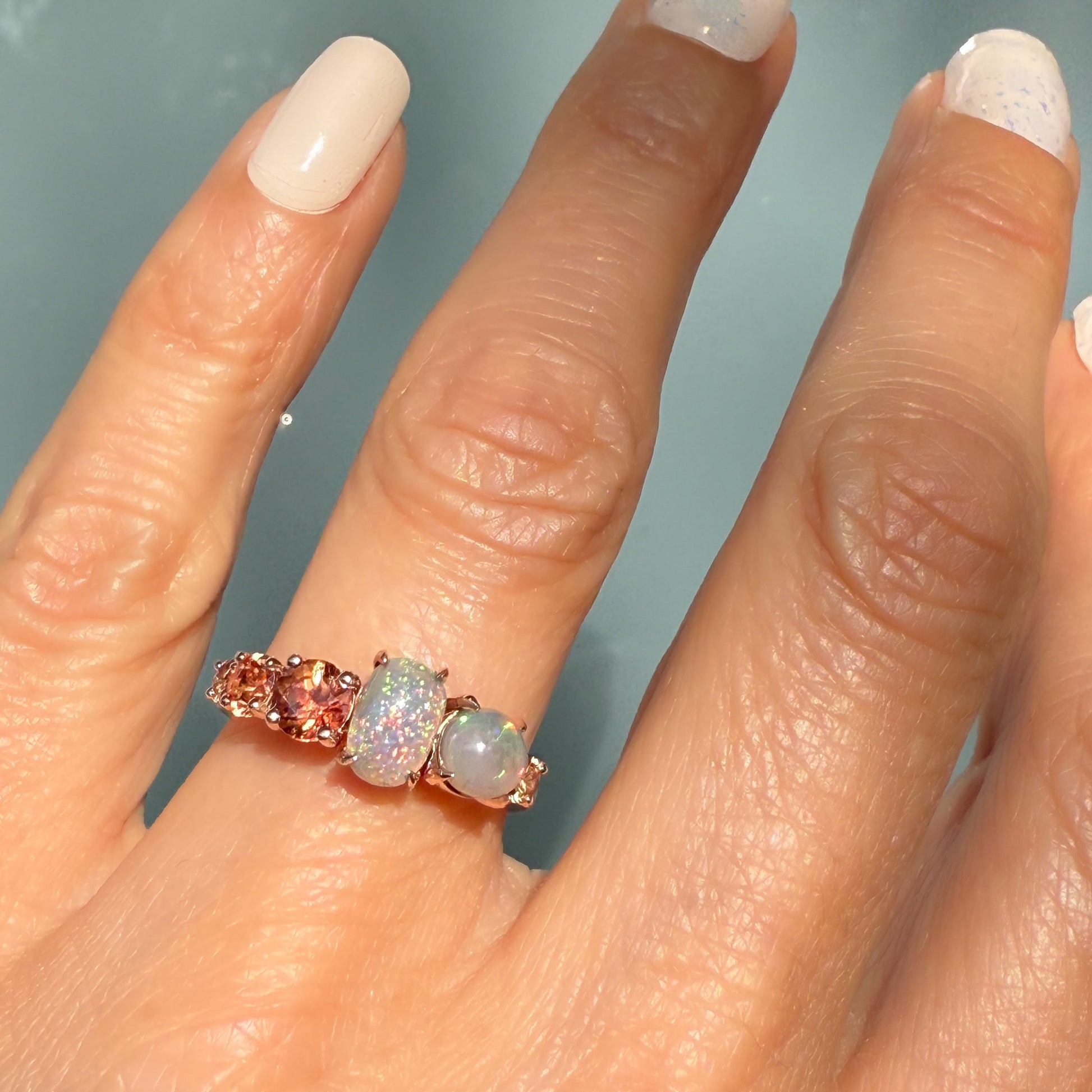 An Australian Opal Ring by NIXIN Jewelry displaying the flawless juxtaposition of semi black opals and round-cut peach sapphires. The prong setting and bright colors make this a highly visible black opal jewelry piece. This luxury ring is a signature NIXIN design.