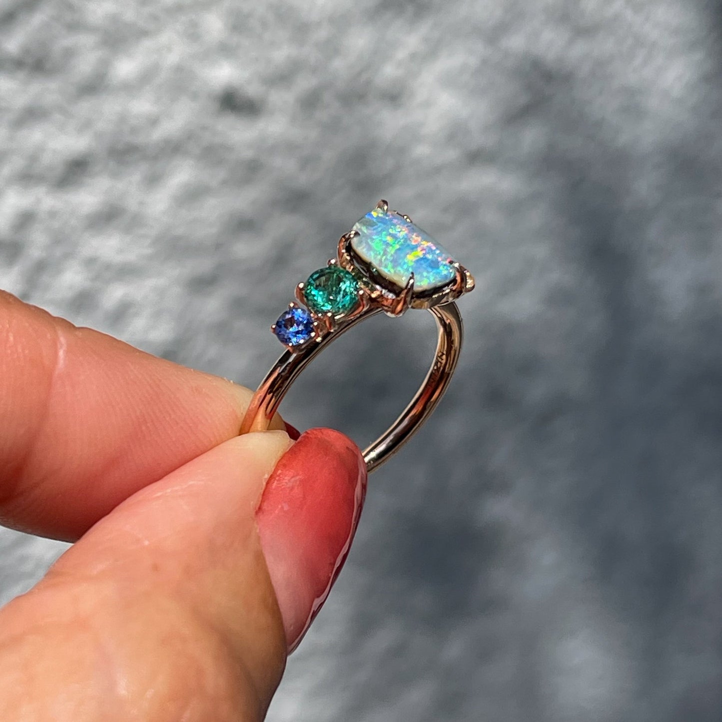 Angled shot of an Australian Opal Ring by NIXIN Jewelry. A blue opal ring with an emerald and sapphires.