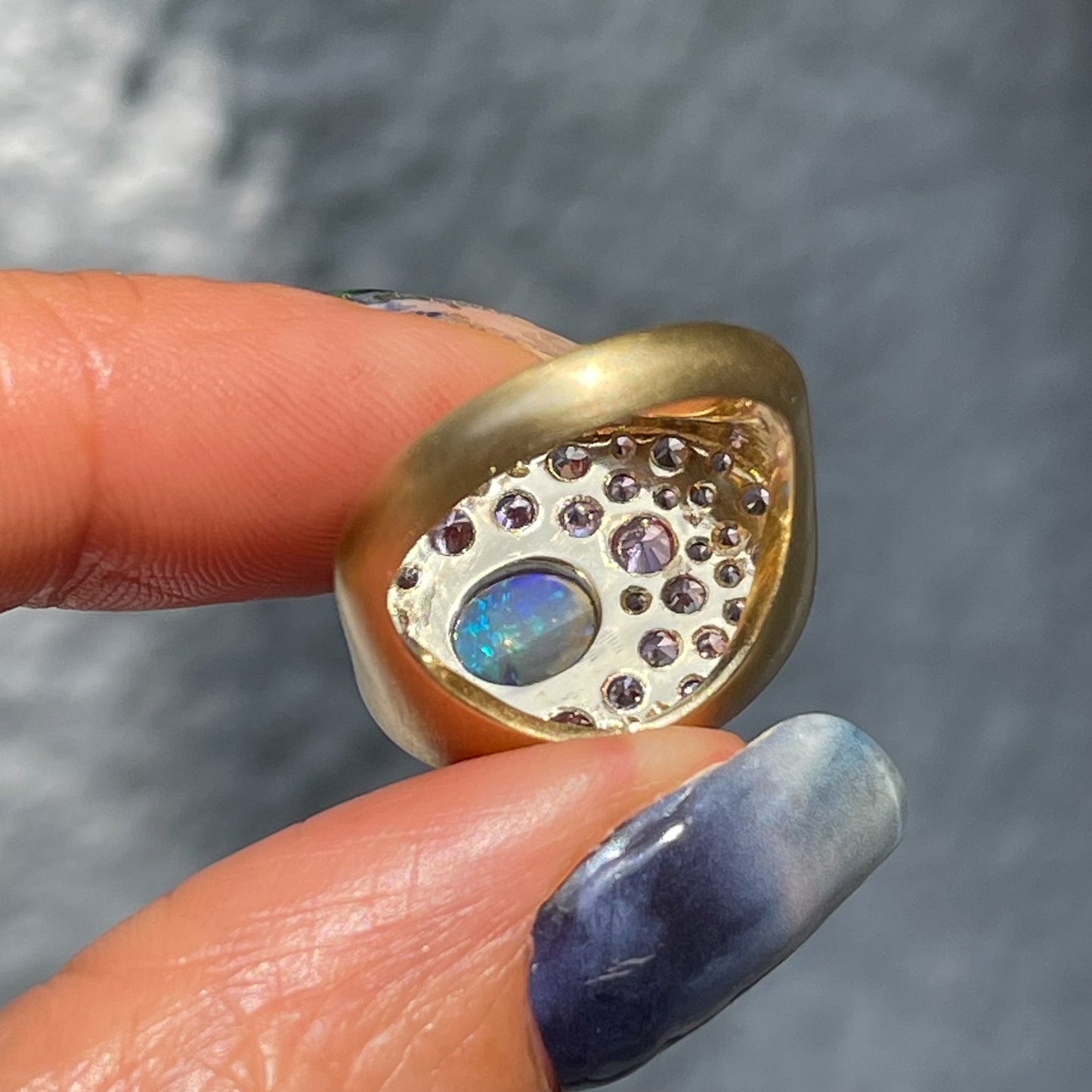 An Australian Opal Ring by NIXIN Jewelry held upside down to show the view of the stone settings from underneath. Exposed culets allows light to travel through the sapphires.