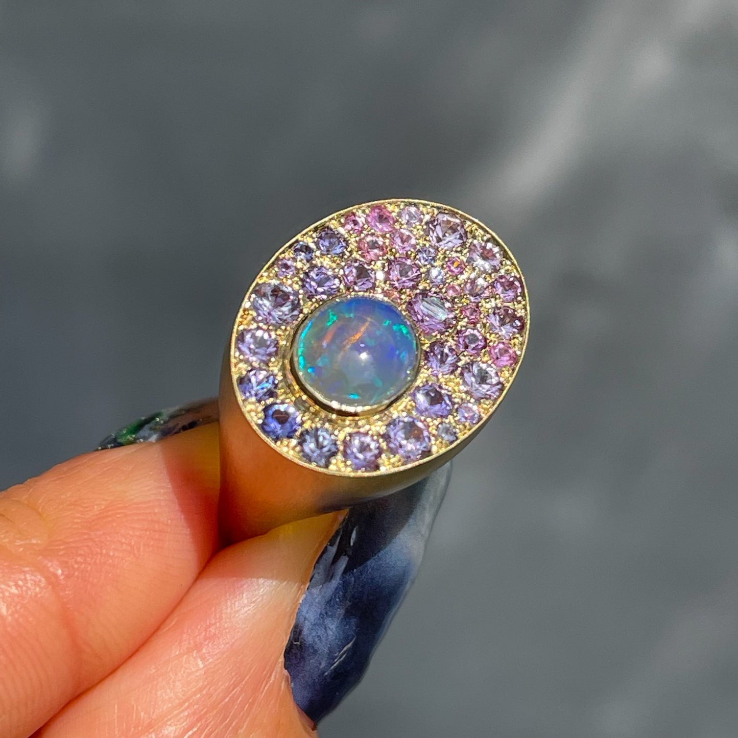 An Australian Opal Ring by NIXIN Jewelry held in front of a grey backdrop. An ombre sapphire ring made in yellow gold with an Australian Opal.