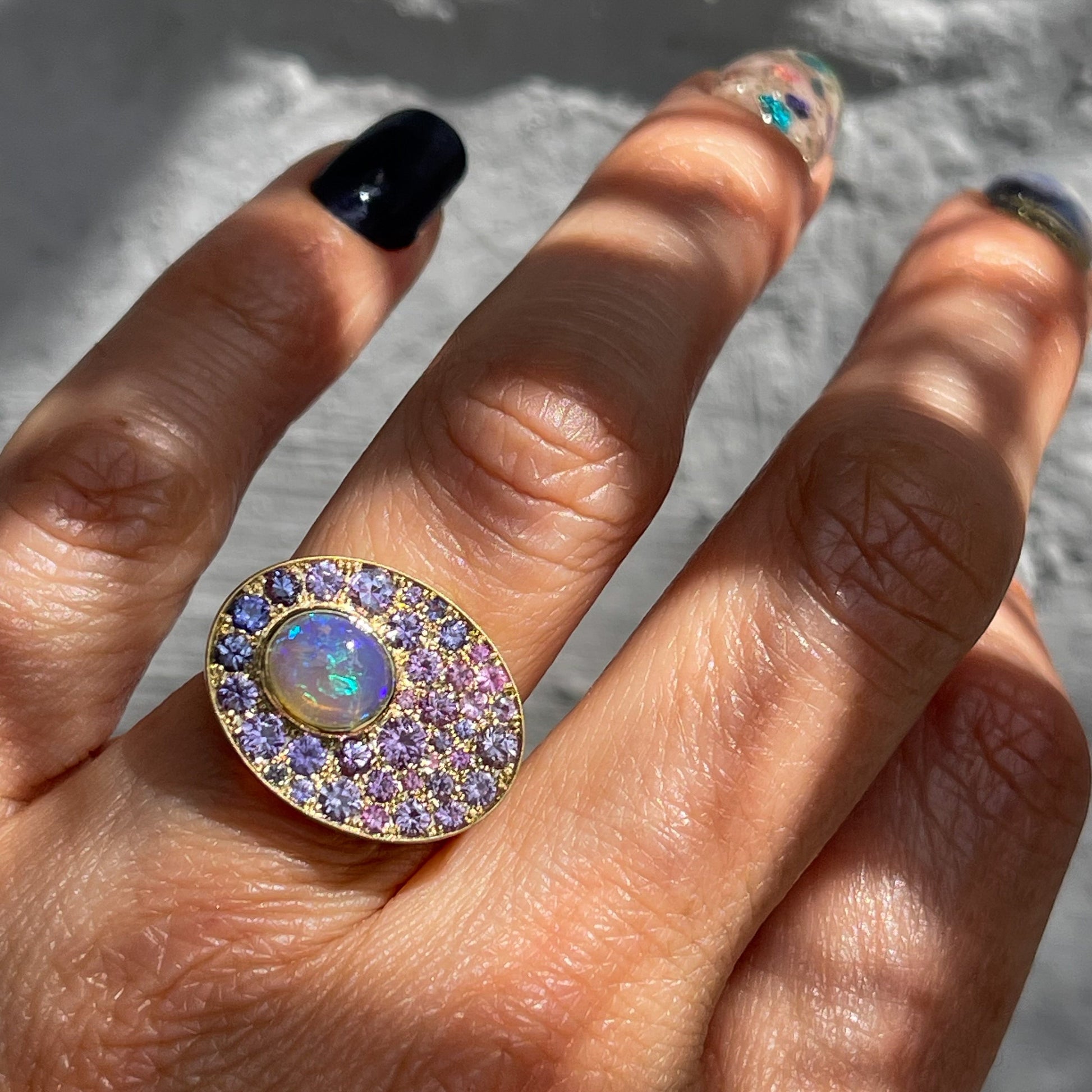 An Australian Opal Ring by NIXIN Jewelry modeled on a hand. The gold opal ring has a Lightning Ridge Opal and purple sapphires and is a one of a kind work of art.