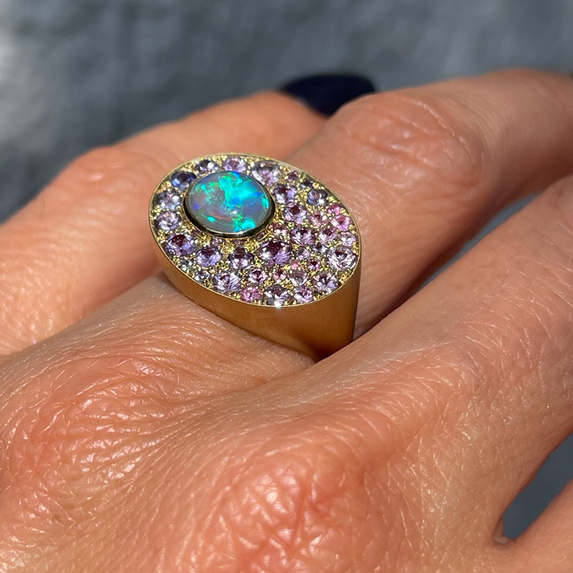 An Australian Opal Ring by NIXIN Jewelry is modeled on the hand and shown up close. Artisan jewelry made with sapphires and opal set in gold.