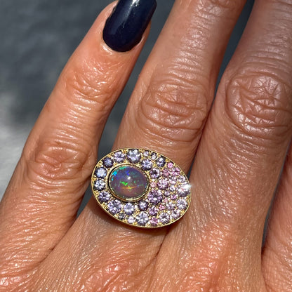 An Australian Opal Ring by NIXIN Jewelry is modeled on the hand in direct sunlight. The purple opal ring is set in yellow gold with a natural opal.
