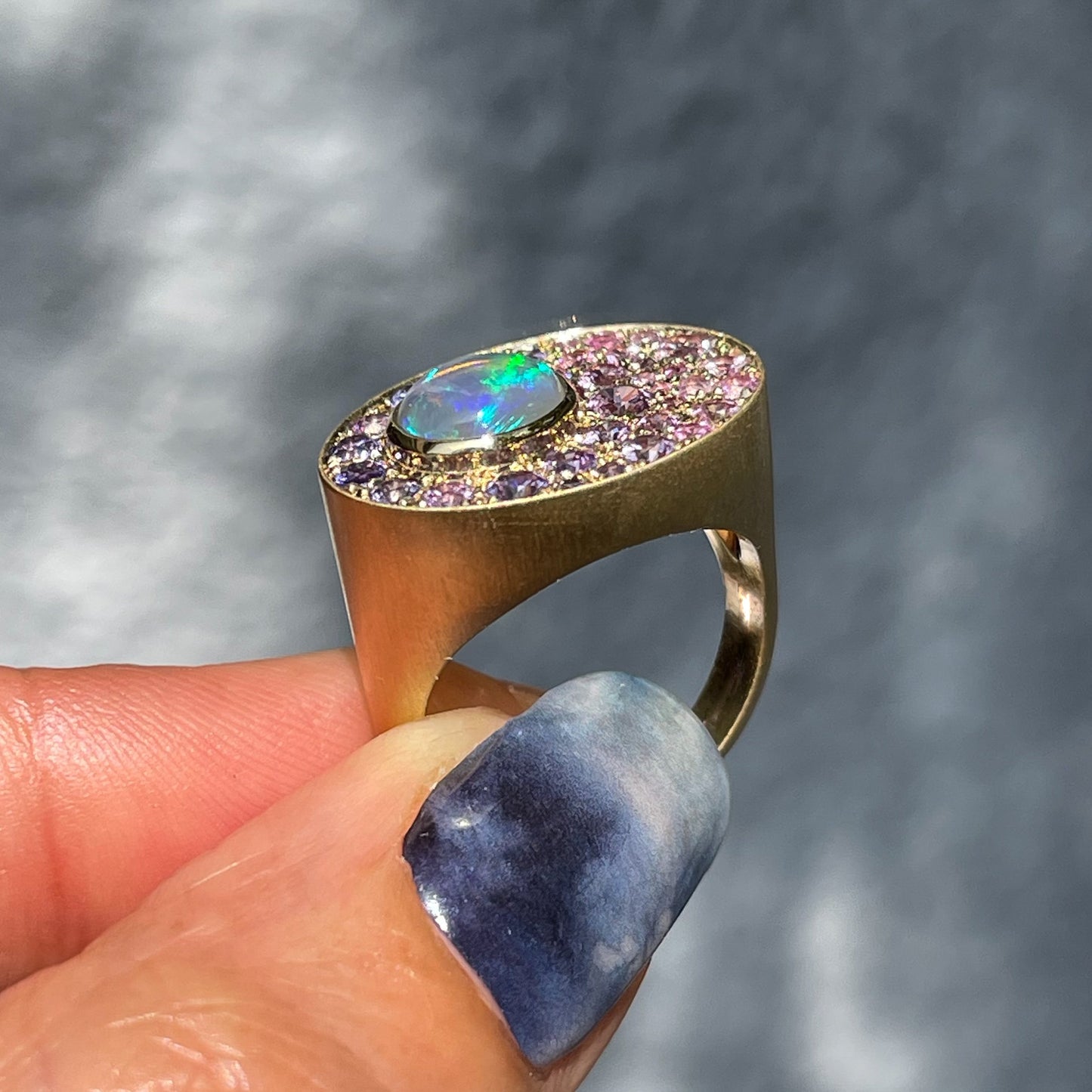 An Australian Opal Ring by NIXIN Jewelry held up to show its profile. The opal signet ring  is made in 14k gold with ombré sapphires.
