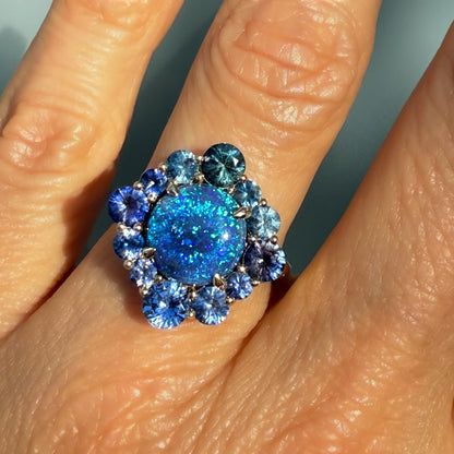 An Australian Opal Ring by NIXIN Jewelry. This captivating top-view shot captures the intense blue opal flash within the black opal, framed by the vibrant sapphire halo. As a striking sapphire opal ring and rare luxury jewelry ring, it represents exceptional unique fine jewelry and art.