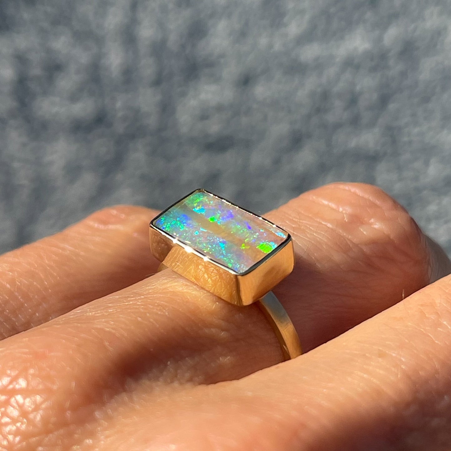An Australian Opal Ring by NIXIN Jewelry modeled with a green opal in a 14k gold bezel setting.