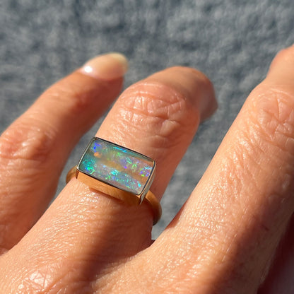 An Australian Opal Ring by NIXIN Jewelry modeled with a blue opal shining from a polished gold bezel.