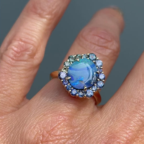 Video of Australian Opal Ring by NIXIN Jewelry modeled on hand. Blue, green and teal sapphires sparkle around a blue opal ring.