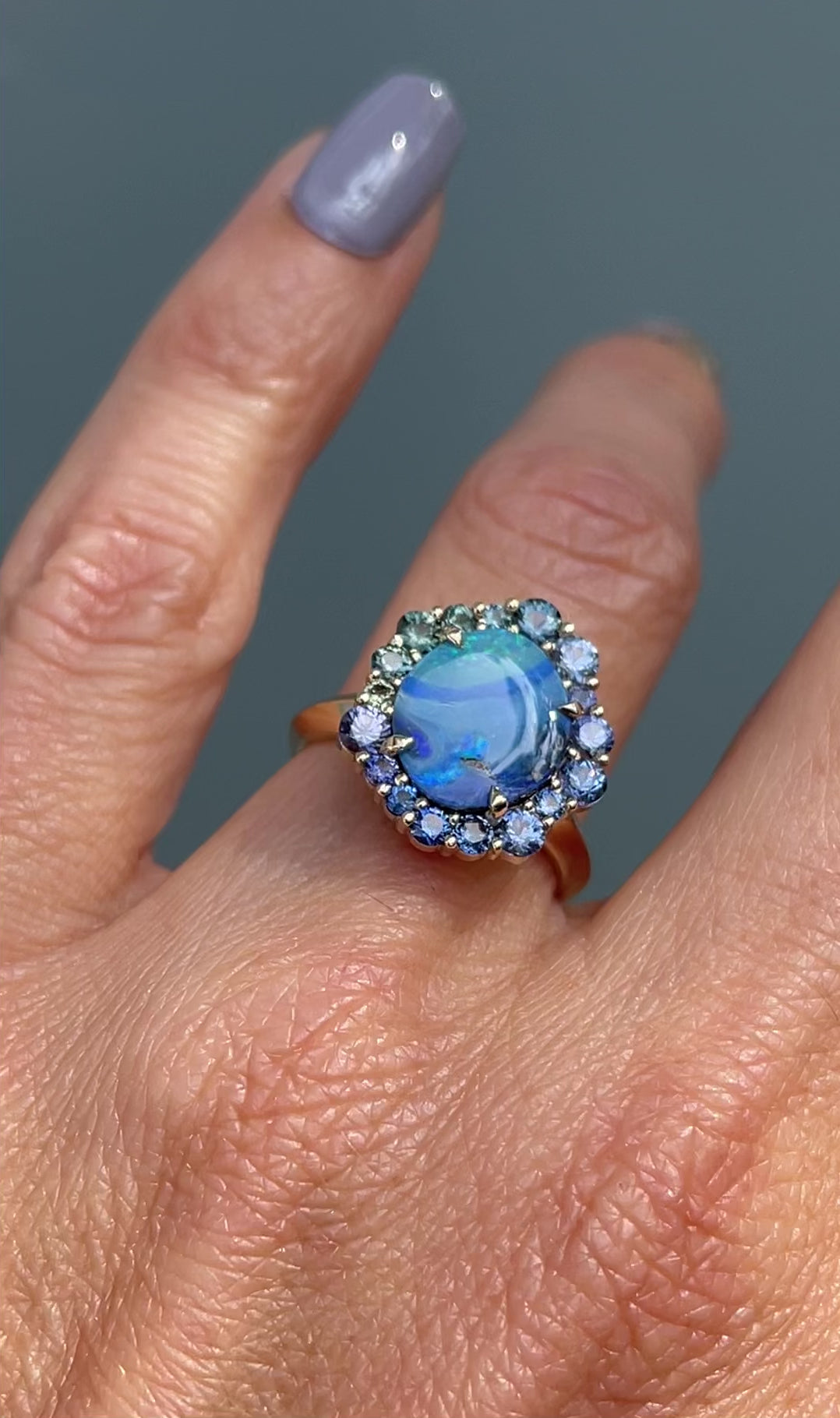 Video of Australian Opal Ring by NIXIN Jewelry modeled on hand. Blue, green and teal sapphires sparkle around a blue opal ring.