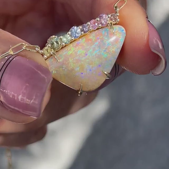 Video of an Australian Opal Necklace held moving between sunlight and in shade. The opal sapphire necklace has ombré gems and is made in 14k gold.