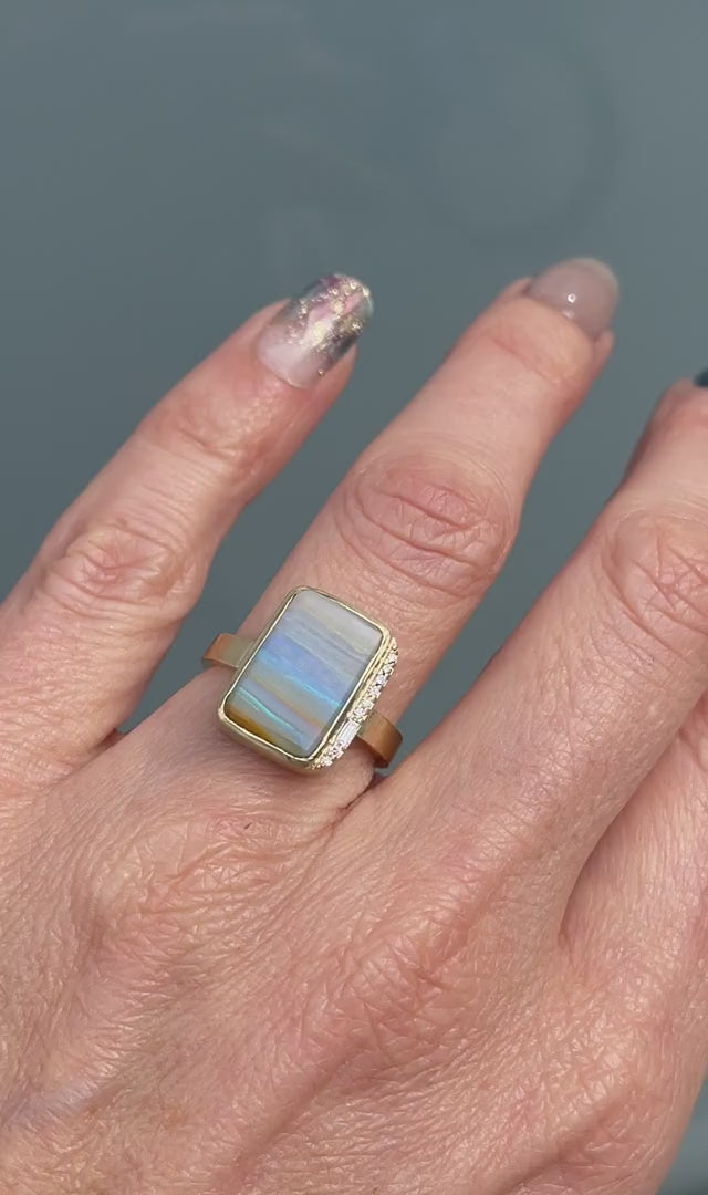 An Australian Opal Ring by NIXIN Jewelry with a blue opal and diamonds set in gold and modeled on a hand to help demonstrate scale.