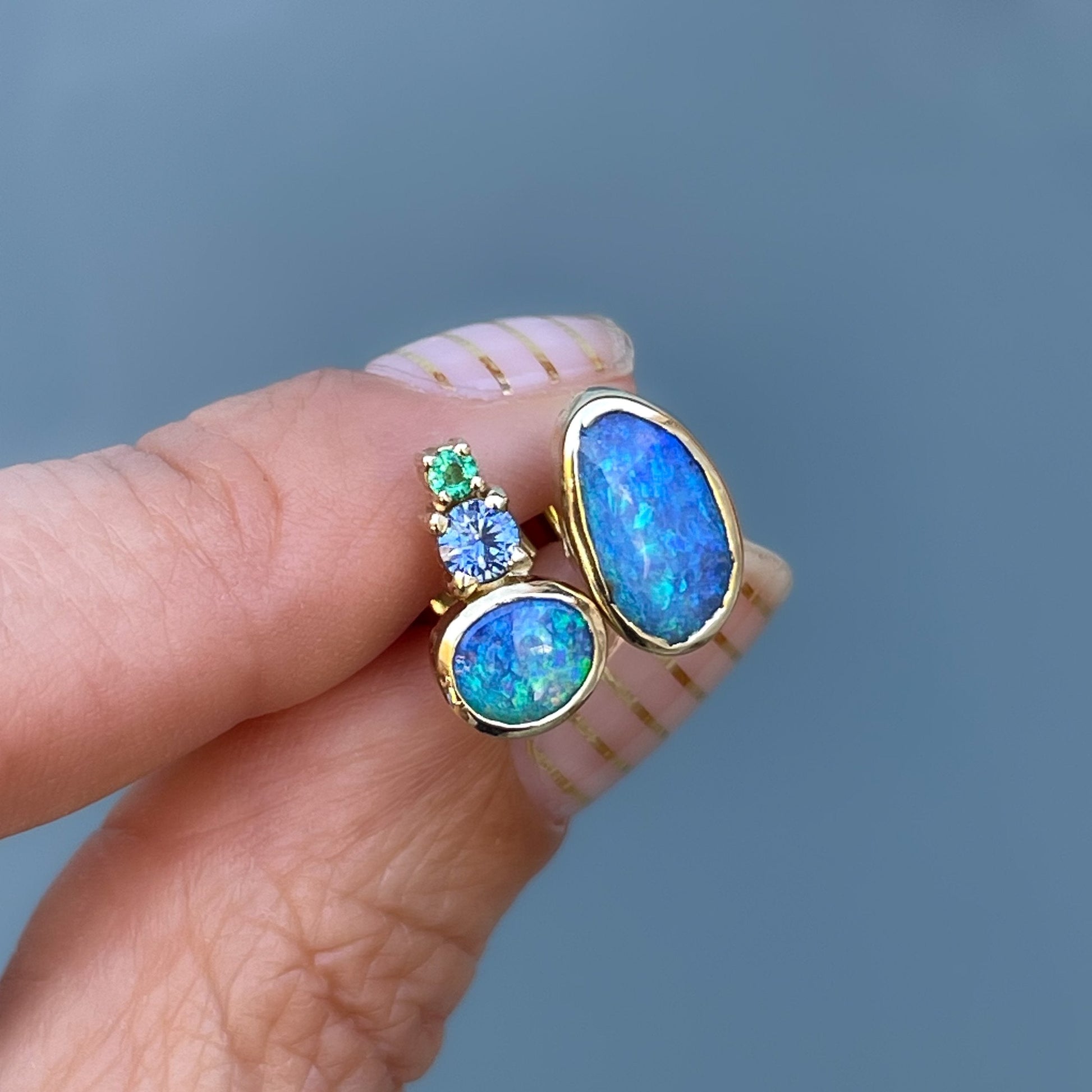 Mismatched opal and emerald earrings held in shade by NIXIN Jewelry