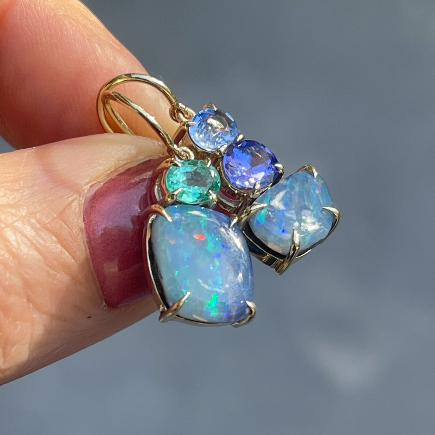 Australian Opal Earrings by NIXIN Jewelry held at an angle in sunlight. Mismatched earrings with blue opals and gemstones.