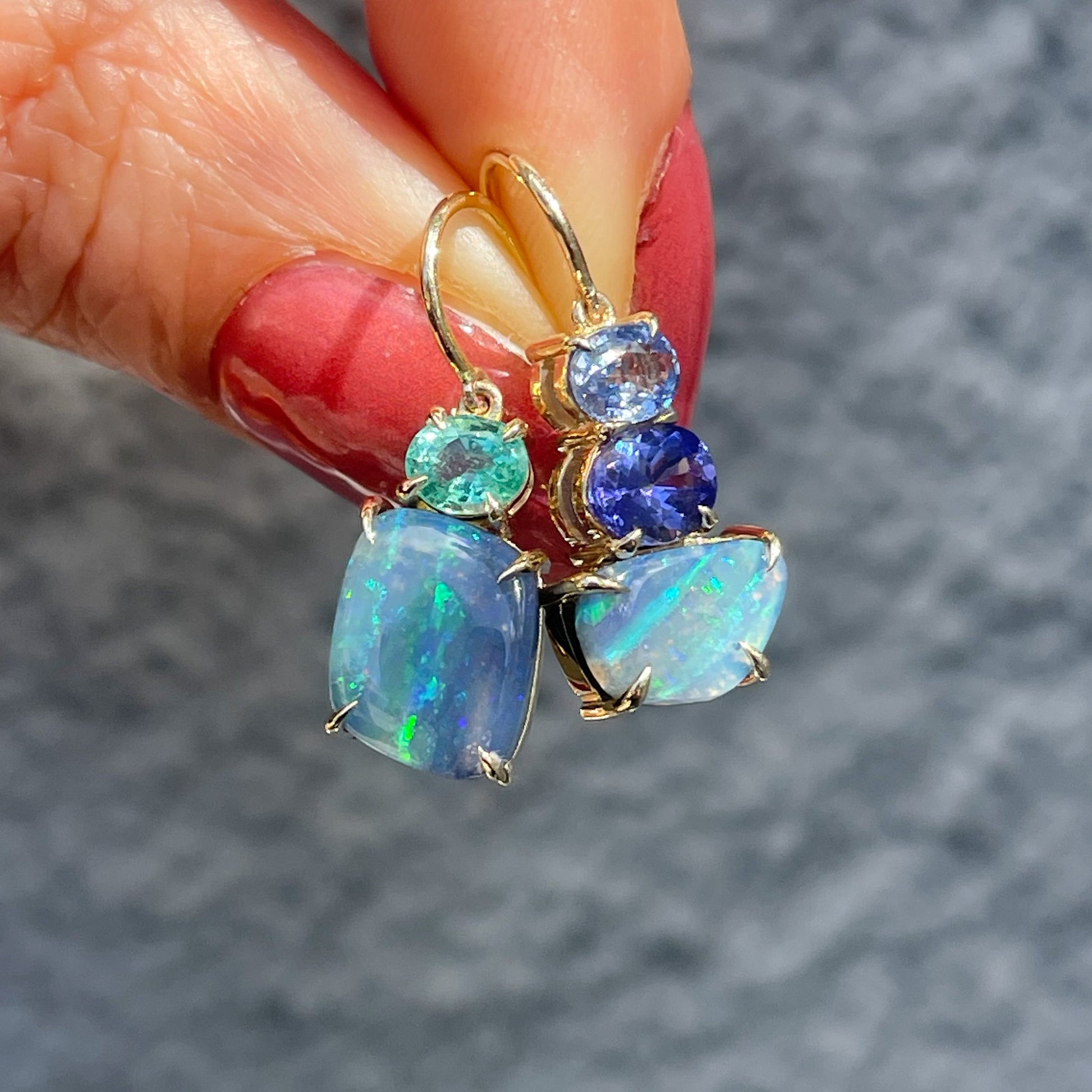 Australian Opal Earrings by NIXIN Jewelry held up in sunlight. Opal drop earrings with emerald and sapphire.
