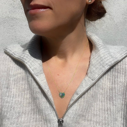 A model is wearing an Australian Opal Heart Necklace by NIXIN Jewelry. The gold opal necklace has a heart shaped Black Opal surrounded by emeralds.