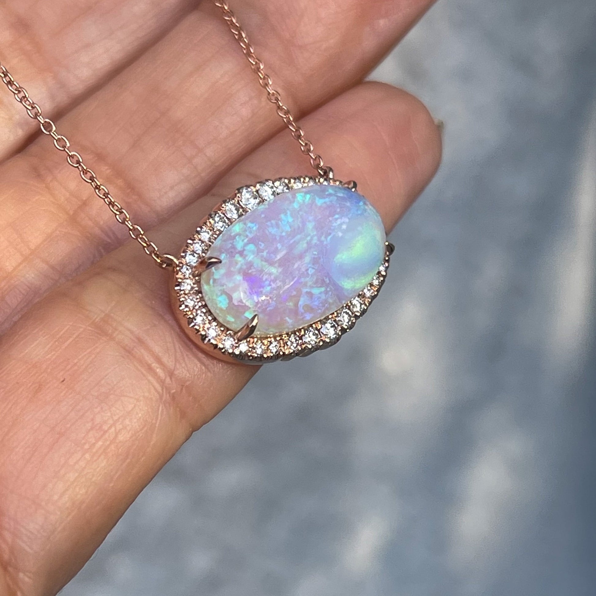 An  Australian Opal Necklace by NIXIN Jewelry shot in shade against a hand. The Crystal Opal shows purple and green with a pave diamond halo.