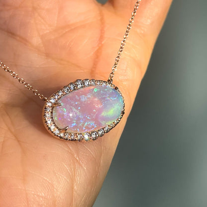  An Australian Opal Necklace by NIXIN Jewelry shot at an angle and resting against a hand. The purple opal is set east west and secured by prong setting.